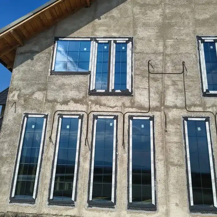Ferestre termopan cu rame negre montate pe o fațadă de casă aflată în stadiu de construcție.