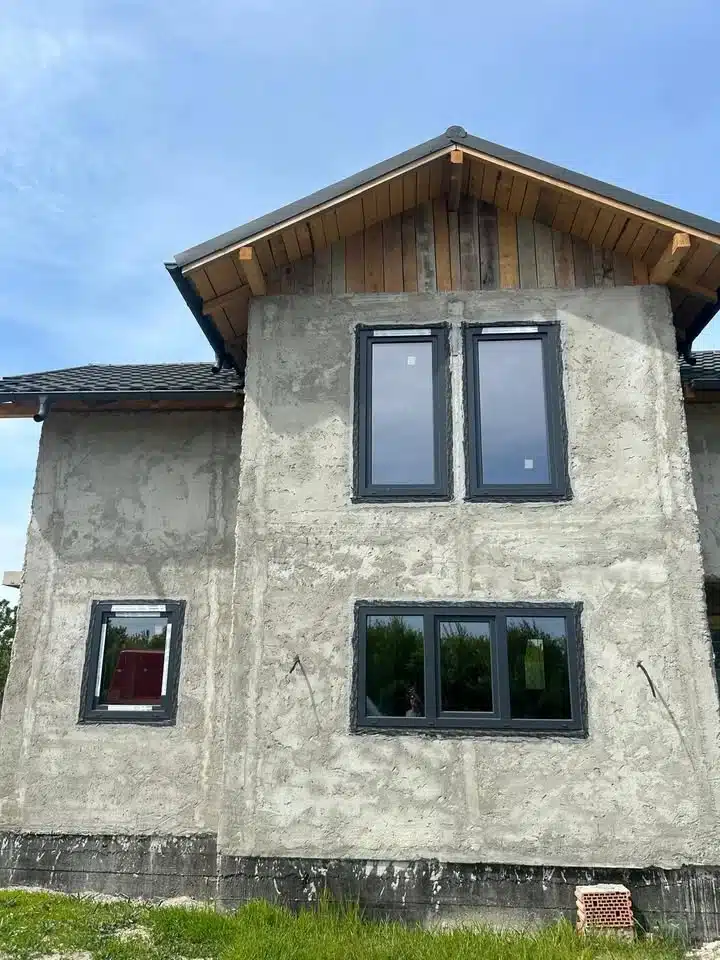 Fațadă de casă în construcție cu ferestre gri antracit montate.
