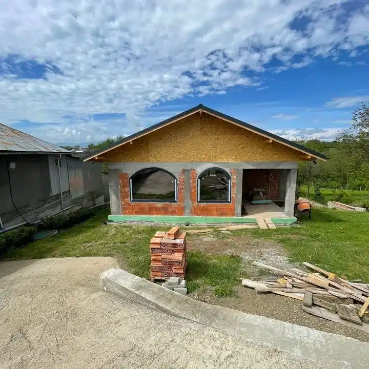 Casă în construcție cu ferestre boltite și zidărie din cărămidă.