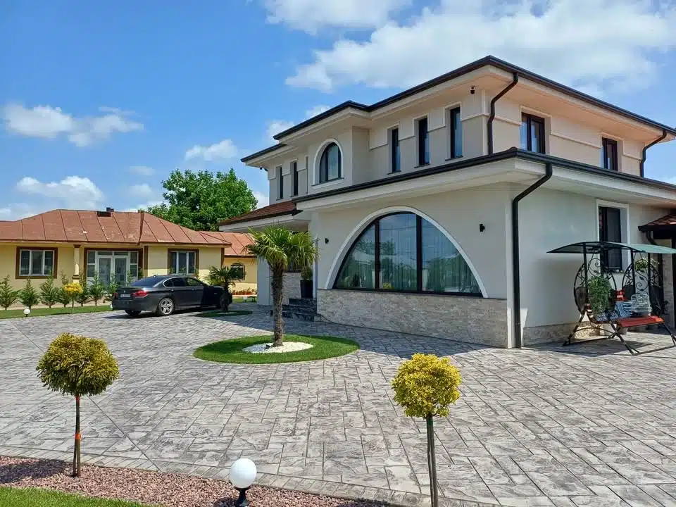 Casă modernă cu fațadă crem, fereastră arcuită și curte pavată cu beton amprentat.